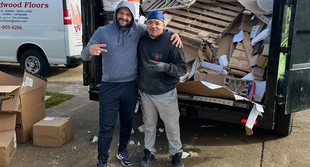 Two men standing in front of a van and a truck filled with junk and boxes on the ground