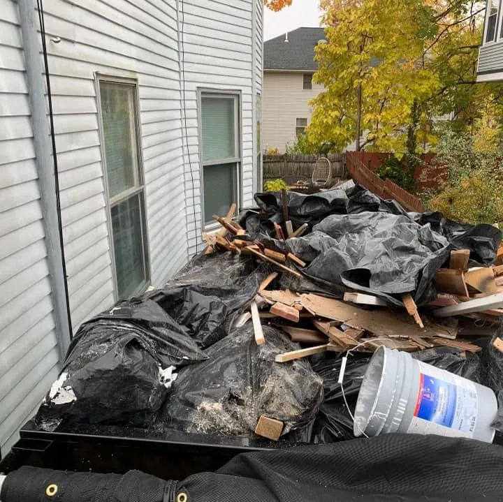 a pile of junk is sitting on top of a dumpster in front of a house